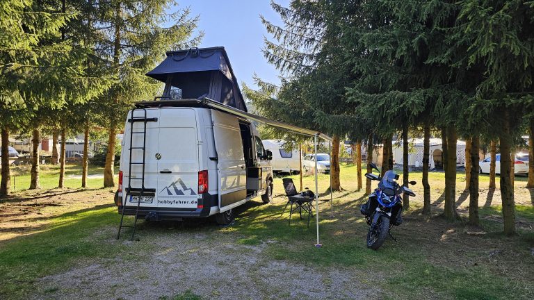 VW Crafter mit Dachzelt und BMW R 1300 GS auf einem Campingplatz am Tag
